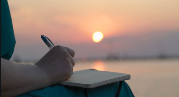 A person sits outside at sunset journaling for cochlear implant.
